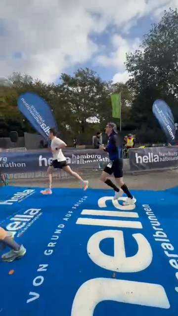 Zwei Läufer in Sportkleidung laufen auf einem blauen Boden mit weißer Aufschrift bei einem Marathon-Event